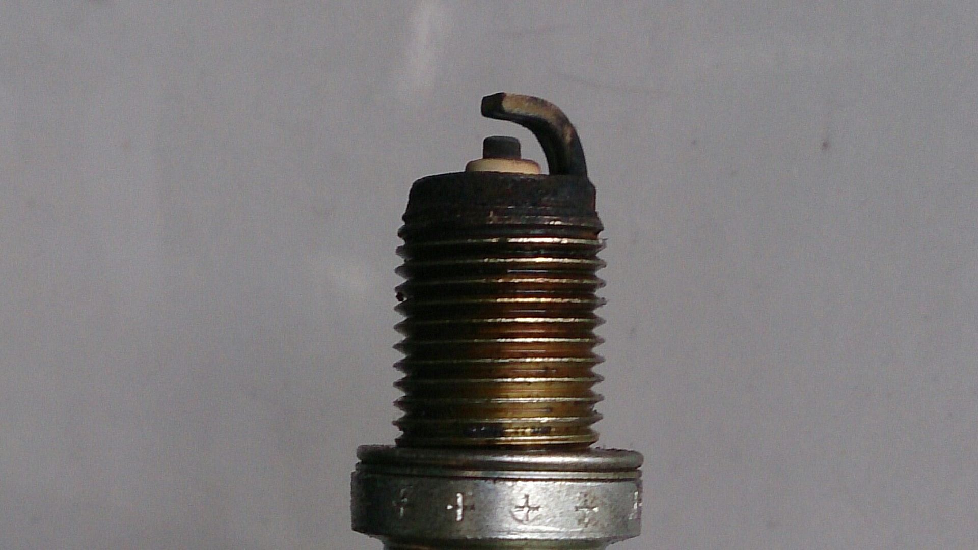 Close-up of a used Denso automotive spark plug showing the ground electrode, threaded shell with visible carbon deposits, and the hex nut.